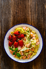 Pasta with baked salmon, cherry tomatoes and dill on wooden table