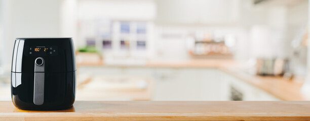 Digital air fryer machine on wooden table in home kitchen