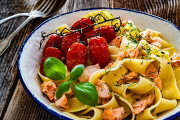 Pasta with baked salmon, cherry tomatoes and dill on wooden table