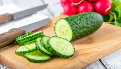 the image shows a wooden chopping block with several pieces of freshly cut vegetables. a green vegetable, partially sliced into several round pieces, sits on the wood surface