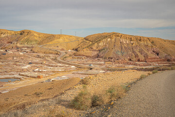 Salt mines in Morocco with earthy yellow and red hills forming a striking backdrop to the industrial landscape under a muted sky