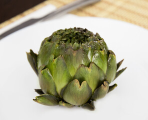 cooked whole artichoke on a white plate