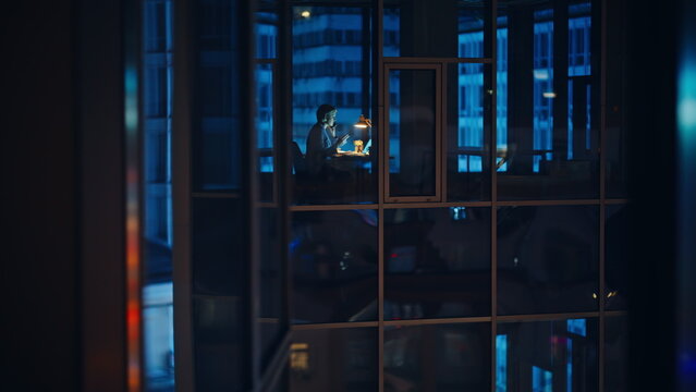Silhouetted businesswoman through window working under lamp light at night hours