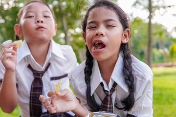 Elementary school girls in school uniform eating snacks and water. Her face looks happy and cheerful. They are sweating from playing and exercising. Concept of childhood fun, friendship, sharing.