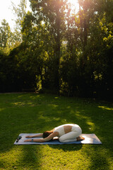 Young woman in sportswear stretching body on fitness mat at public park, doing yoga. Healthy lifestyle, sport. Fitness. Girl doing yoga in morning park. Part of a series. Soft focus