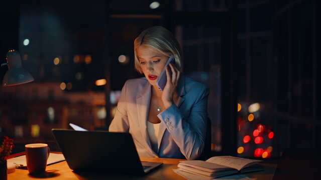 Overworked blonde talking cellphone searching documents computer table closeup