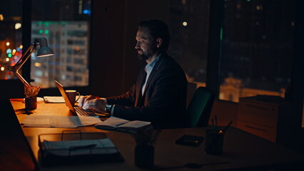Man manager working late at night office. Serious businessman typing laptop