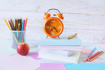 Back to school concept. Alarm clock, stack of books, apple, colored pencils and pastel colored paper on white wooden background.