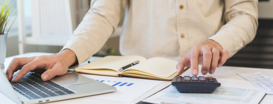Account finance, asian young business man hand using calculator, laptop computer for calculate budget, cost and income of company from paperwork, plan spend money expenses, working on desk at home.