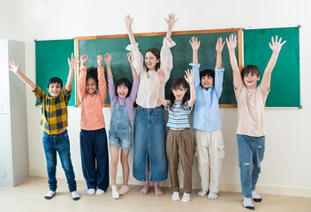 Diverse group of cheerful school children standing together in front of a chalkboard, linking arms...