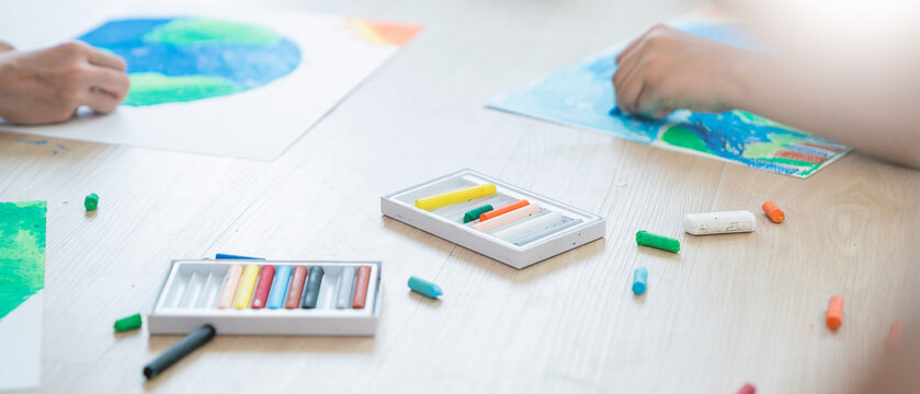 Group of kids hands drawing with crayons on the floor during an art activity in a bright classroom setting. Education back to school earth day concept
