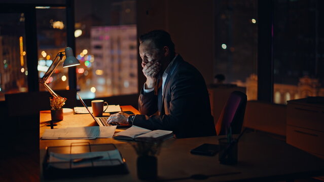 Yawning director typing laptop dark workspace closeup. Manager checking contract