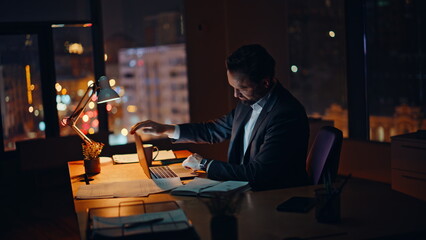 Late manager working pc at company workspace. Tired businessman closing laptop