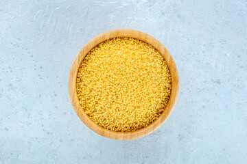 Millet, ancient African grain, in a wooden bowl on a blue background, overhead flat lay shot. Healthy vegan side dish