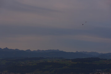 Two hot air balloons drift over a vast, layered mountain landscape at sunset, conveying a sense of adventure, freedom, and scale.