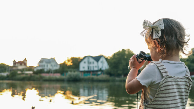 A little girl looking through binoculars near a lake at sunset.