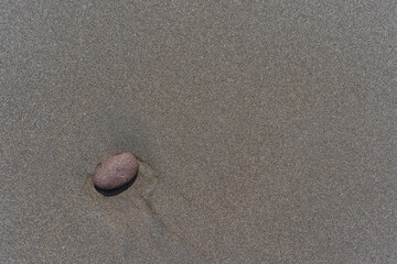 Black volcanic sand as a background. A small pebble, smoothed by water. Beach on the Pacific Ocean