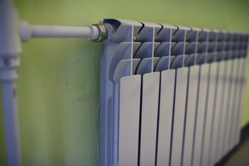 White modern aluminum radiator battery for hot water heating, on the background of a wall in the interior of an apartment or office space.