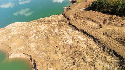 Aerial view of a brown earth excavation site near a calm water body, showcasing ongoing...