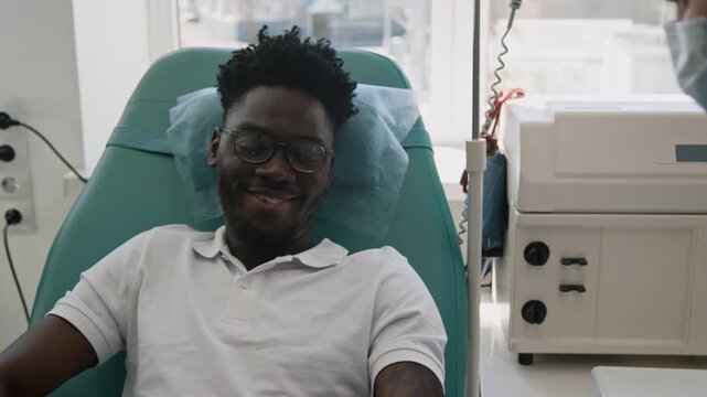 Tilt-up over the shoulder shot of African American man receiving medical care, while donating blood, from healthcare professional in clinic