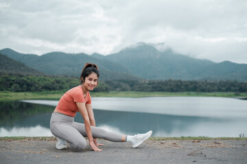 Fototapeta premium Woman in activewear stretching by a lake with mountains in the background, showcasing fitness and nature.