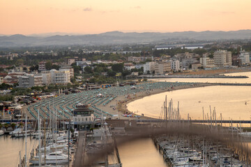 Fototapeta premium Seaport of Italian city of Rimini. Wide sandy sea beach resort with sun loungers and umbrellas on coast top view. Hotels apartments. Port Italy