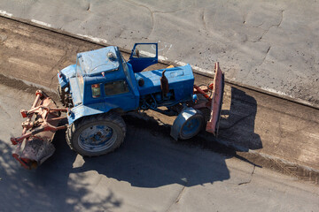 Obraz premium This high-angle shot of a classic blue tractor with a rear-mounted sweeper brush and an open door is perfect for a designer needing a vintage or utilitarian aesthetic for projects related to road main