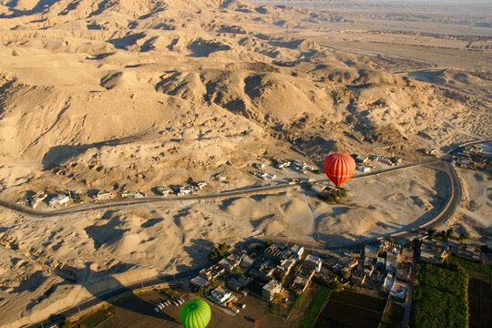 A serene morning scene with multiple hot air balloons soaring above, casting long shadows over the landscape and houses