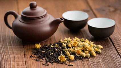 Traditional teapot with dried chrysanthemum flowers and black tea on rustic wooden table, calm herbal tea preparation scene