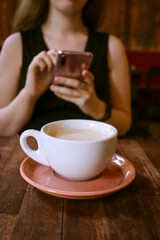Cozy cafe scene with a steaming cup of coffee in focus and a blurred woman in the background.