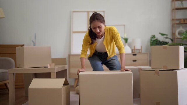 Asian adult woman lifting heavy moving box new home relocation effort struggling unpacking items house moving difficulty property move challenge apartment