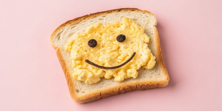 A slice of bread topped with scrambled eggs and a smiley face on a pink background