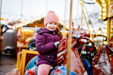 Adorable little girl riding merry-go-round carousel horse at Christmas funfair outdoors. Happy child enjoying traditional family Xmas market in Nuremberg, Germany © Irina Schmidt