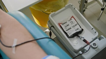 Close-up shot of unrecognizable arm resting on armrest with needle inserted, connected to blood bag during blood donation process in clinic - Powered by Adobe