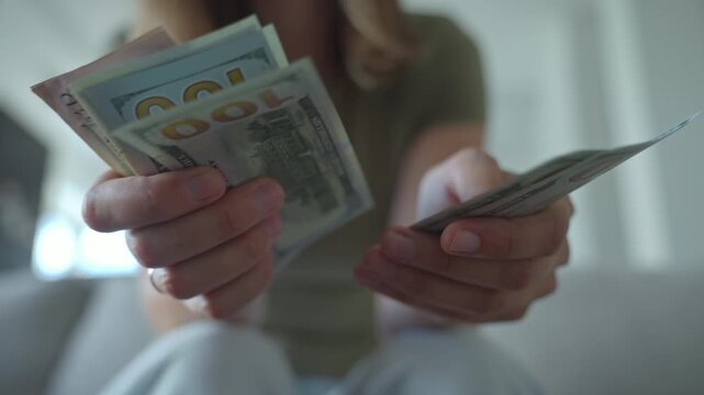 Woman holding and counting US dollar banknotes in hands. Concept of personal finance and savings