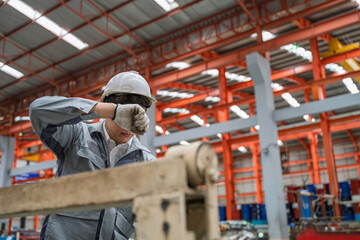 Industrial worker operating a metal sheet machine in a factory. Safety helmet and gloves show...