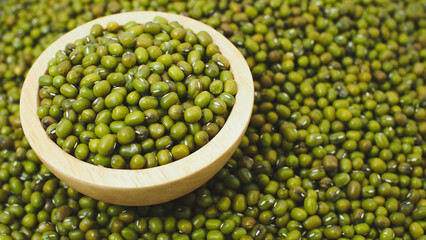 Closeup of raw green mung beans in a wooden bowl placed on a pile of beans background. Ideal for illustrating healthy food