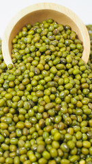 Mung beans spilling from wooden bowl on white background