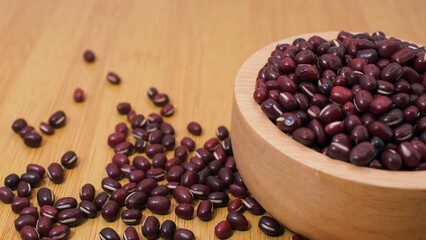 Close-up of red adzuki beans in a wooden bowl with scattered beans on wooden background, symbolizing healthy eating, plant protein, and Asian cuisine ingredients.