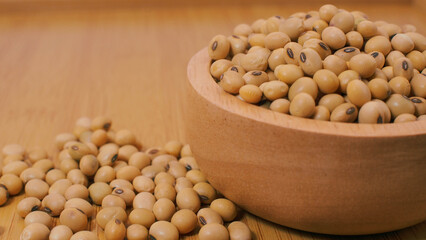 Close-up of soybeans in a wooden bowl with scattered beans on a wooden surface, symbolizing...