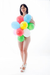 Playful nude woman holding colorful balloons in front of her body, celebrating on white background