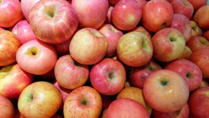 This is a close-up shot of a large pile of apples. The apples are a mix of red and pink with hints of yellow and green, suggesting a variety like Gala or Fuji.