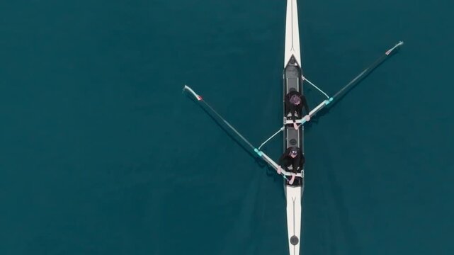 Two athletes rowing a sculling boat on calm blue water, teamwork and endurance in competitive sport. Rowers are practicing sport rowing. Rowers in a racing boat row in slow motion video 120fps.