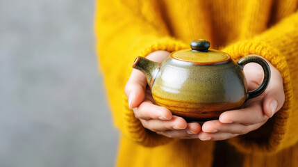 Thanksgiving gratitude expressed through hands gently holding ceramic teapot with warm colors and cozy yellow sweater background