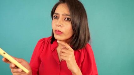 Confused thoughtful South Asian woman with yellow phone looking at the camera - Powered by Adobe