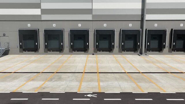 Drone view of modern warehouse loading docks with empty bays, marked lines, and striped pavement