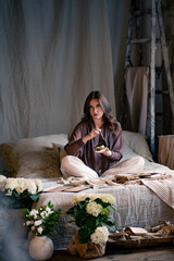 Obraz premium Beautiful young woman posing with singing bowl and sadhu boards in vintage room on bed, many flowers around bed, beautiful vintage interior. Yoga practice, sound healing, esotericism
