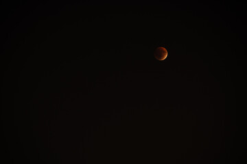 In a clear night sky, a mesmerizing partial lunar eclipse displays a reddish hue on the moon. Stars twinkle softly in the background, accentuating the celestial beauty above