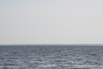 The tranquil water spreads out towards the horizon, reflecting a clear sky. A distant shoreline is subtly visible, creating a serene atmosphere