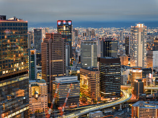 Illuminated cityscape of Osaka at dusk, featuring skyscrapers, highways, and urban lights, Japan.